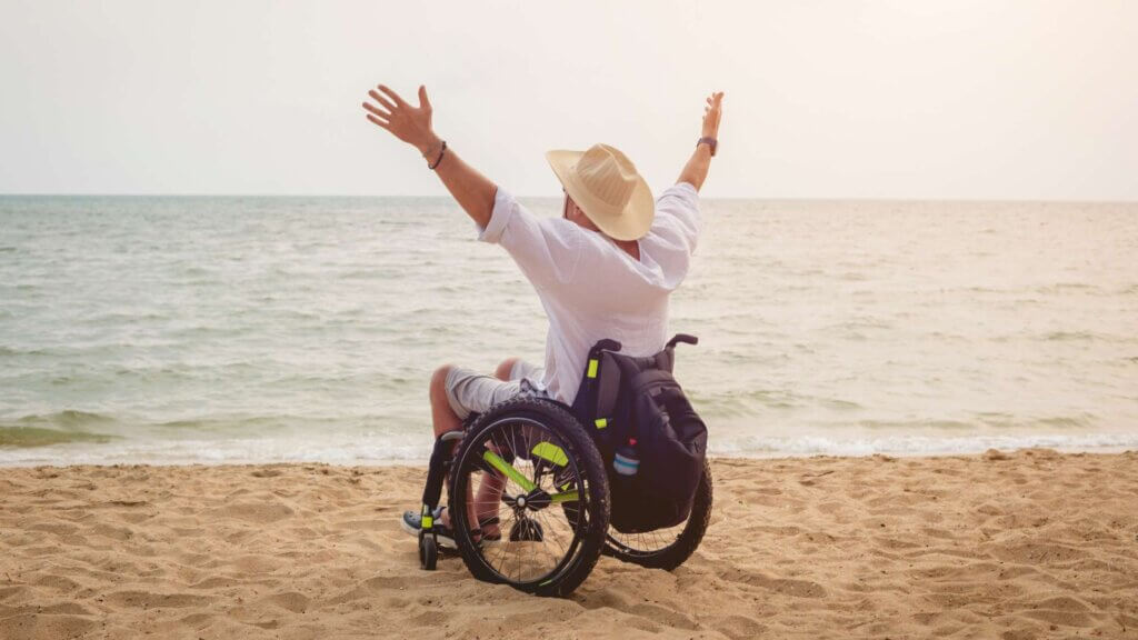 Uomo in sedia a rotelle felice con le braccia al cielo in spiaggia