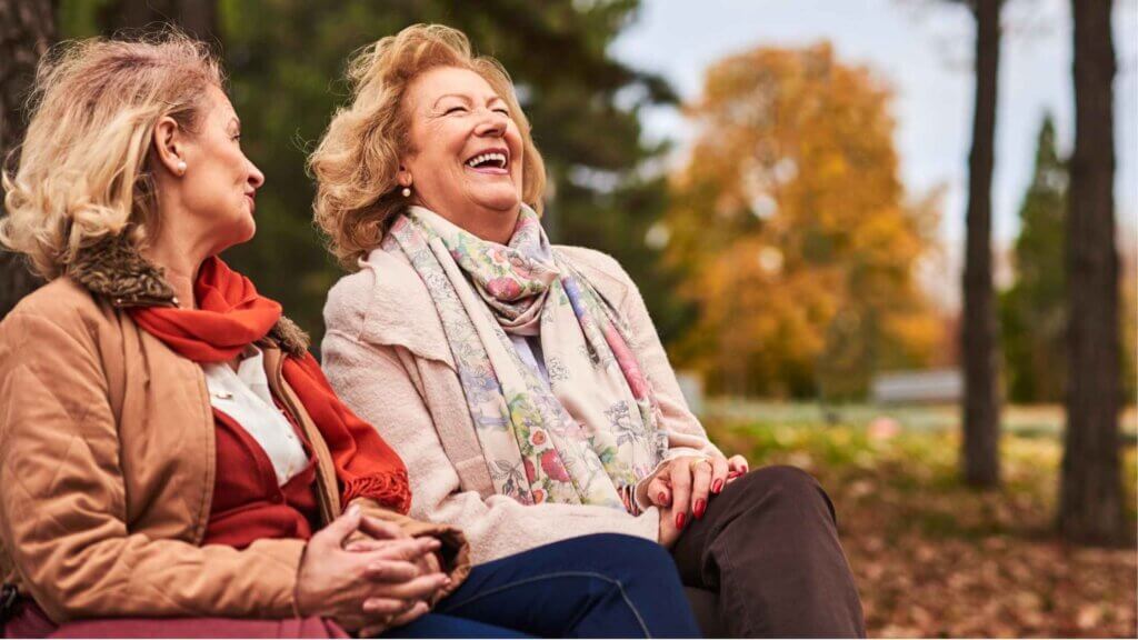 Due anziane felici sedute su una panchina al parco