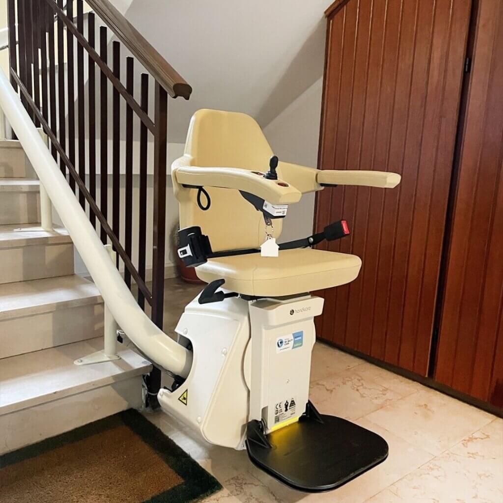 Montascale a poltroncina installato su scala interna, con seduta imbottita pieghevole e guida laterale.