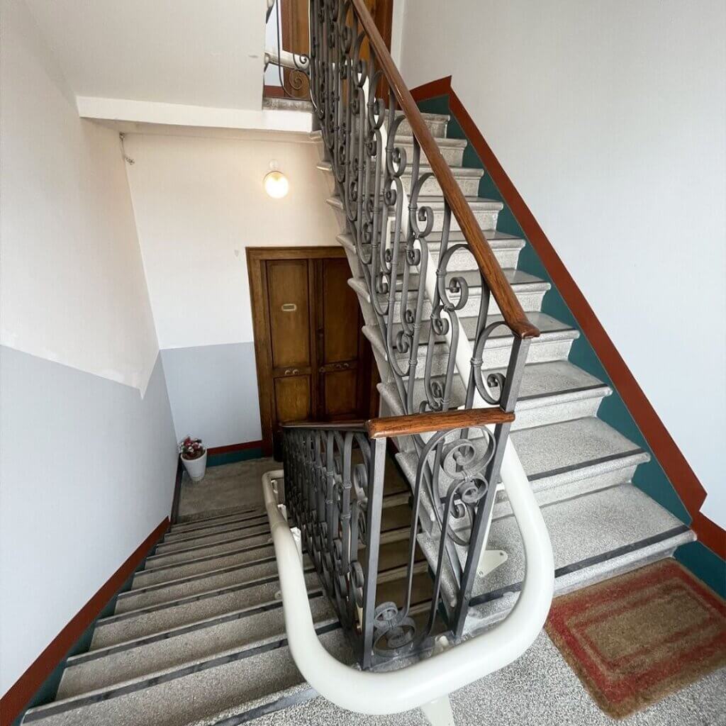 Montascale a poltroncina su guida curva installato in scala condominiale per agevolare la mobilità e superare le barriere architettoniche.