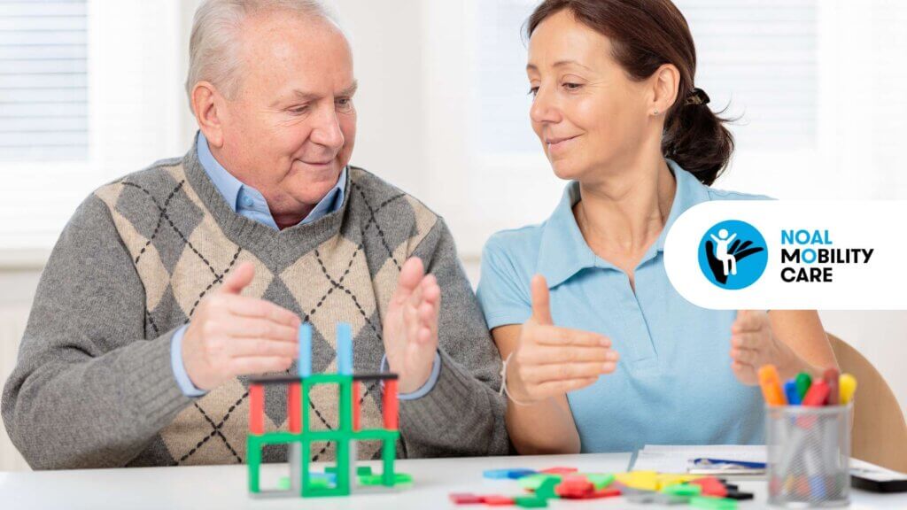 Terapista occupazionale assiste un anziano durante un’attività cognitiva e motoria con strumenti riabilitativi su tavolo.