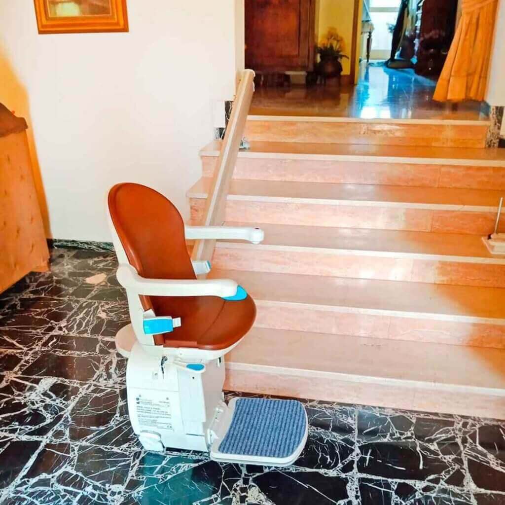 Un montascale a poltroncina ai piedi di una rampa di scale all'interno di un'abitazione